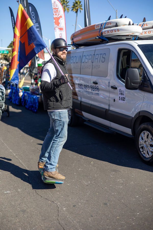 Justin Ostrom holds a Onewheel AZ flag while moving next to the Riverbound Sports van in the parade.